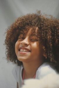 Bambina con capelli ricci naturali che sorride con sicurezza.