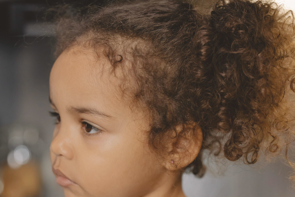 Primo piano dei capelli ricci di una bambina con capelli più corti visibili vicino all’attaccatura
