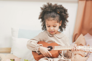 Bambina con capelli ricci naturali raccolti mentre suona un ukulele