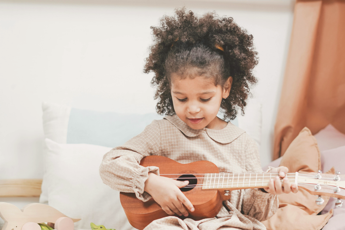 Bambina con capelli ricci naturali raccolti mentre suona un ukulele